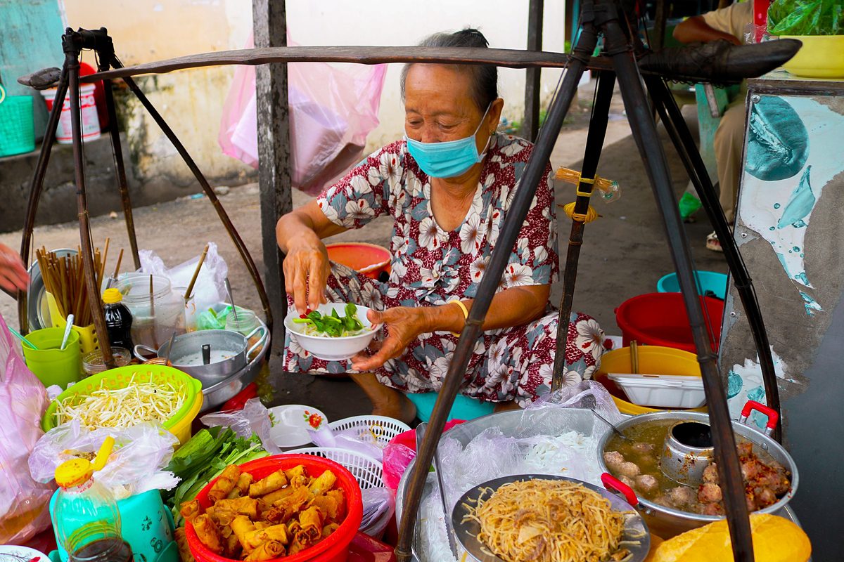 Banh tam bi is often regarded as a popular street food dish in the Mekong Delta, Vietnams rice basket, because of its delicious and appealing taste. On a tour of An Giang that borders Cambodia, dont forget to visit this stall located near Long Hung crosscroads in Tan Chau Town where an old woman has been serving this dish on her shoulder pole. Without a signboard, advertising or table, her stall has been going strong for more than 20 years.