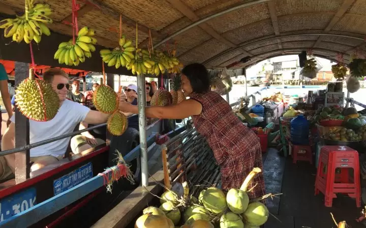 Tourists buying some fruits from a boat on Cai Be floating market Tourists buying some fruits from a boat on Cai Be floating market